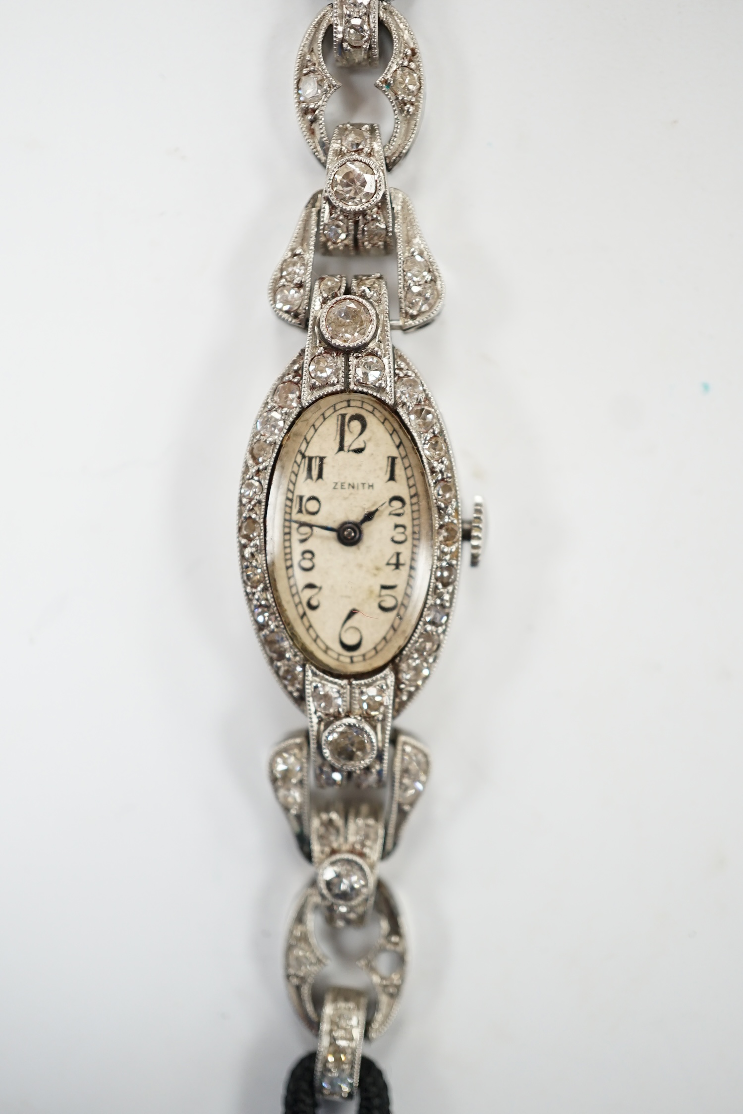 A lady's Zenith white metal and diamond cluster set manual wind oval cocktail watch, on a twin fabric strap, 15cm, gross weight 16.7 grams. Fair condition.